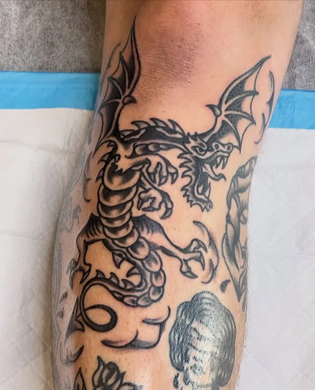 Fresh traditional dragon tattoo fitted under the knee, surrounded by healed work